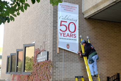 UW-Madison carpenter Bruce Steinhofer installs the WCER 50th anniversary banner