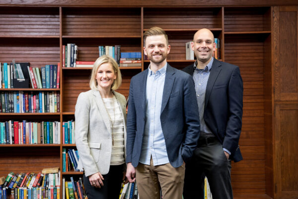 Katie Eklund, Steve Kilgus, and Andy Garbacz, the leaders of the School Mental Health Collaborative (SMHC) pose together in front of a bookcase.